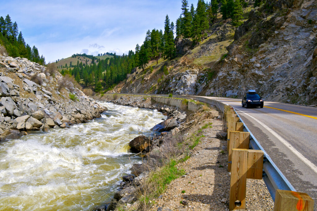 A lone automobile is seen traveling on Idaho State Highway 55 adjacent to the lower North Fork of the Payette River near the tiny town of Banks in Western Idaho. The world class rapids are one of the most challenging river rapids in North America due to snow melt runoff from high up in the Sawtooth and Salmon River mountains, over 150 miles away. Western Idaho, Western USA.