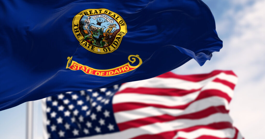 The Idaho state flag waving along with the national flag of the United States of America on a clear day. 3D illustration render. Rippled fabric. Selective focus