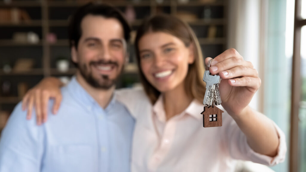 Close up blurred joyful millennial loving married couple showing keys to camera, celebrating purchasing own apartment or feeling excited of renting new dwelling, real estate agency service concept.