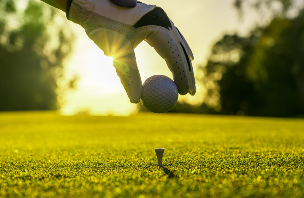 Closeup of golfer wearing glove placing golf ball on tee at golf course