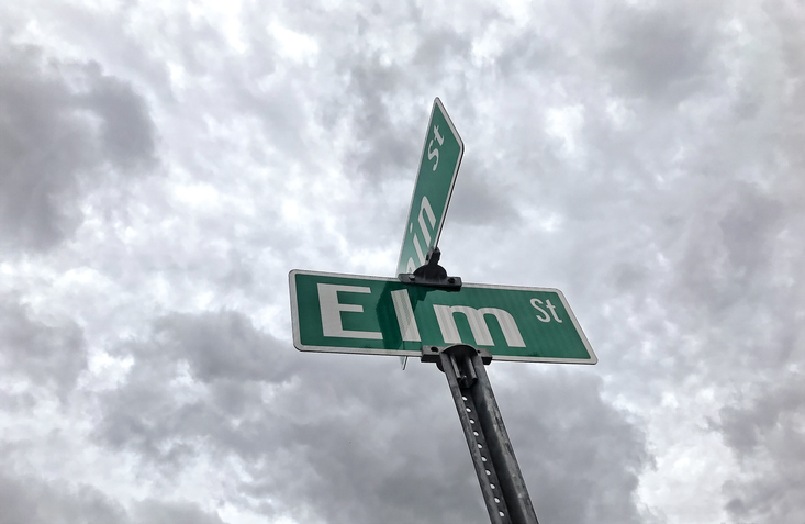 Elm Street Road sign in front of a cloudy sky