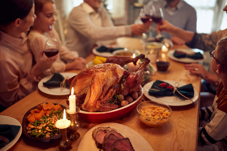 Closeup of roast turkey at dining table on Thanksgiving with family toasting in the background.