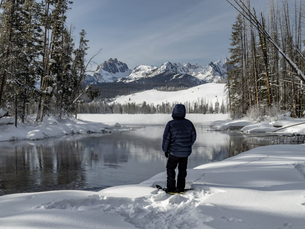 Winter snowshoer take a break along a riverside in winter to enjoy the view of mountains